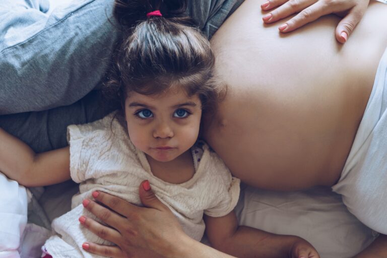 Beautiful Pregnant Woman And Her Cute Little Daughter Together In Bed